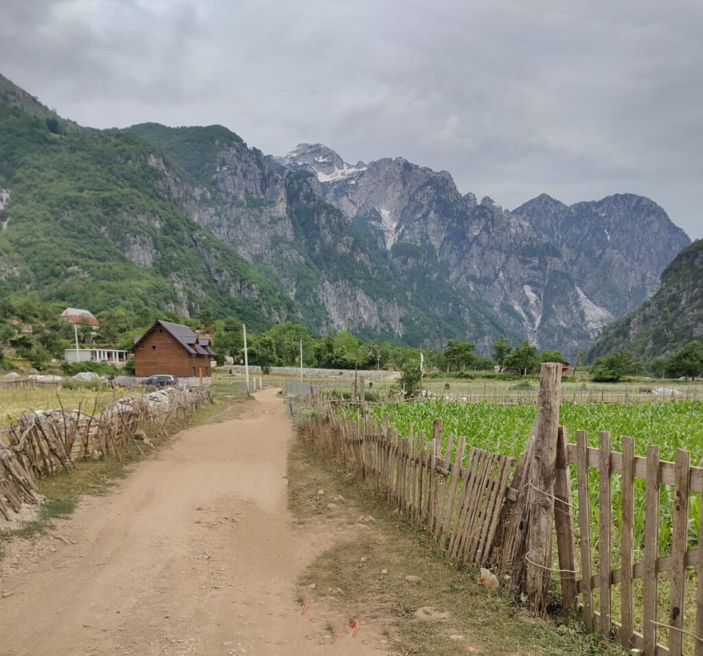 A path in the open fields of Theth village with mountains around