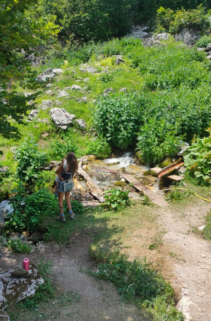 A mother with a baby by a fresh water river stream on the Theth Valbona hiking trail  
