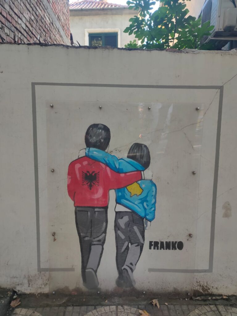 A Graffiti from the Streets of Tirana of two kids with shirts representing Albania and Kosovo Hugging 