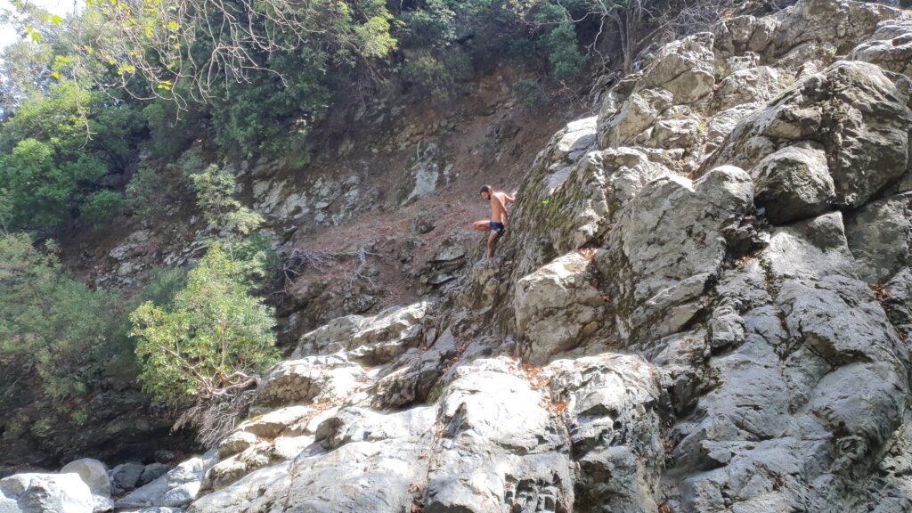 A man climbing down the rocks in the woods of the hippie island of Samothraki