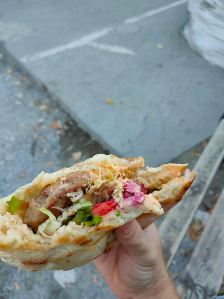 A hand holding Pita Kebab in the market of Pristina